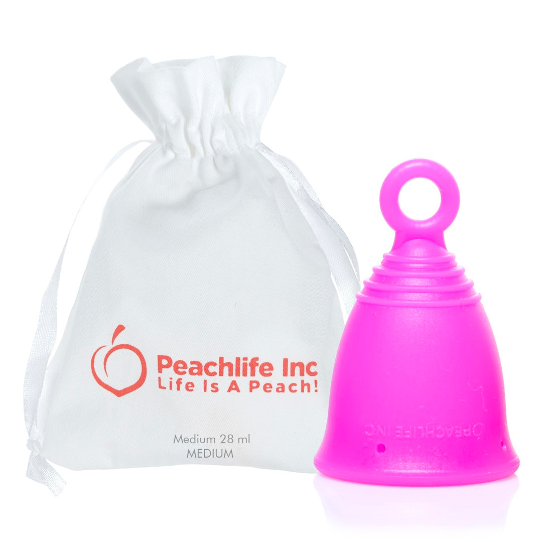 A bright pink menstrual cup with a loop handle next to a white drawstring pouch printed with the brand name 'Peachlife Inc' and the slogan 'Life Is A Peach!' on a white background.